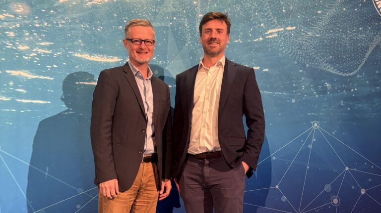 Arnaud Ayral, chief commercial officer, SolarDuck, and Cameron McNatt, managing director, Mocean Energy stand together at the signing of the MOU in front of a background depicting the ocean