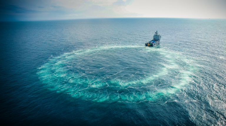 A diagram of a bubble curtain being deployed in a ring in the ocean. The curtain is a light green colour compared to the darker ocean waters
