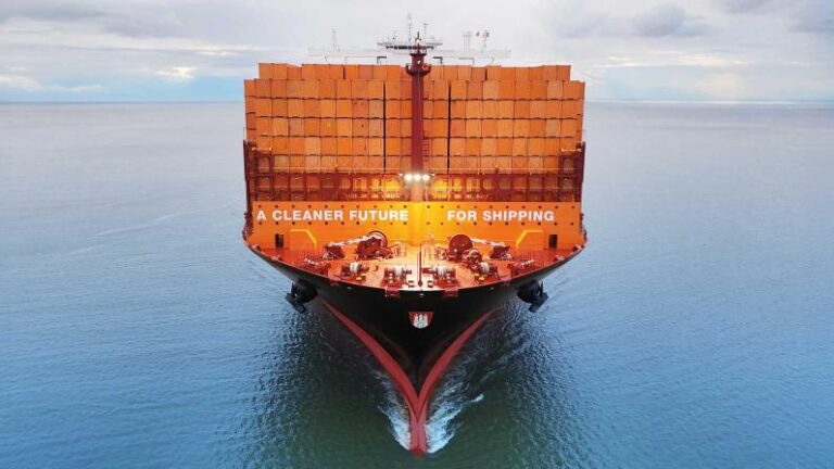 A container ship loaded with orange containers sails across a calm sea